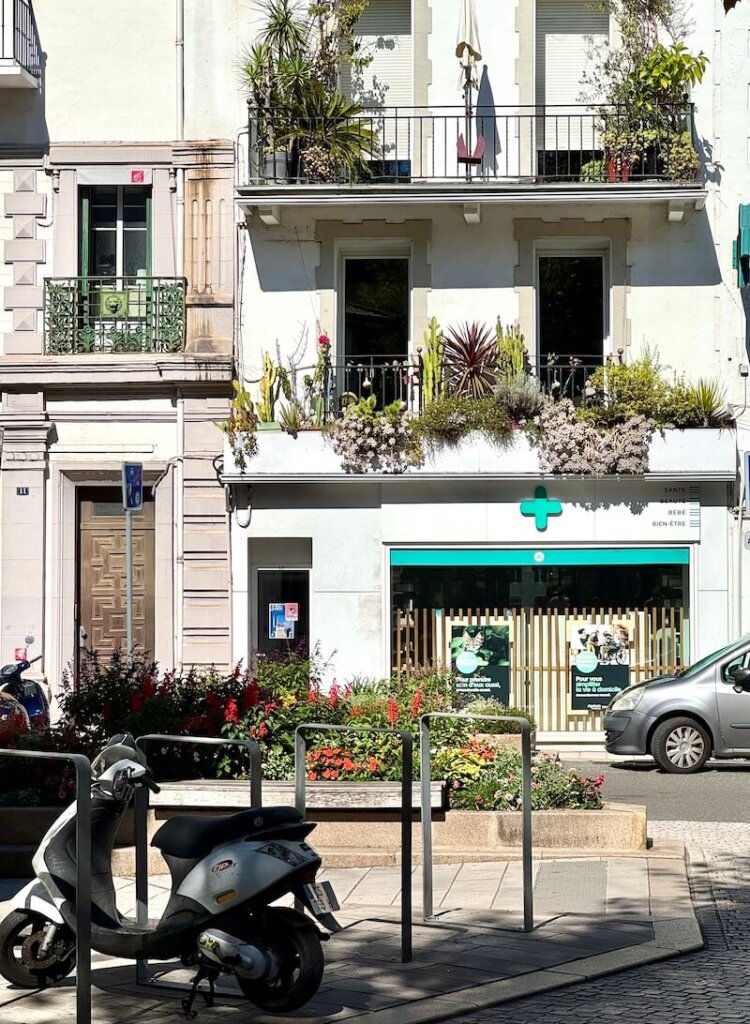 One of the buildings in downtown St Jean de Luz a pharmacy with flowers and plants growing on it and also a scooter in front