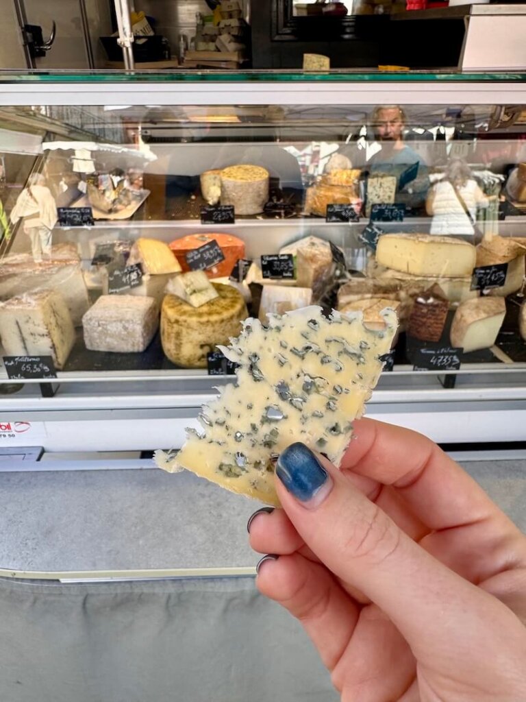 Allison's hand holding a piece of cheese while at a market in Samatan France