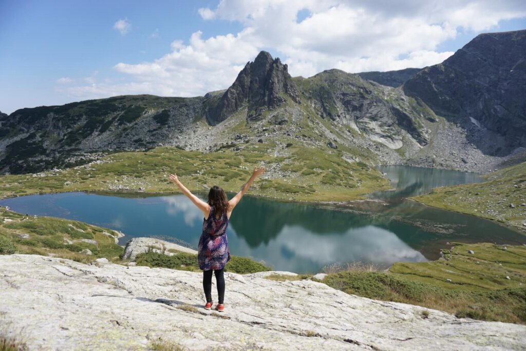 Allison Green standing with her hands held up to the sky rejoicing at the beauty of the Rila Lakes