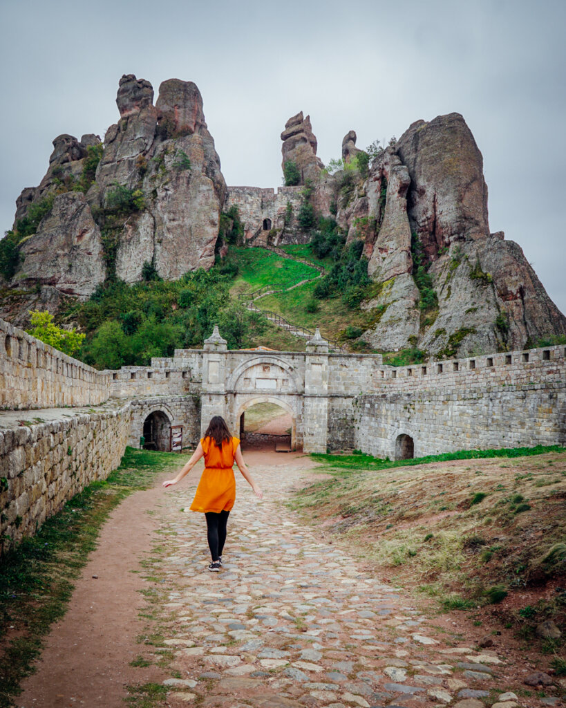 Allison Green wearing an orange dress and black leggings while visiting Belogradchik Fortress