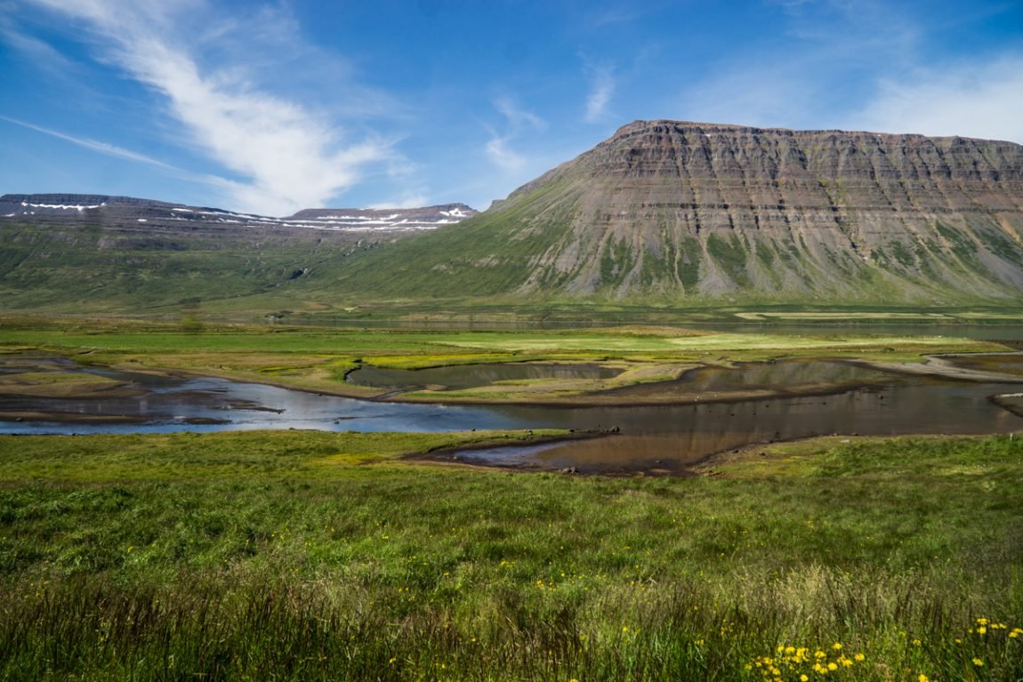 The terrain of the westfjords with river and highish mountains behind it in sanda valley