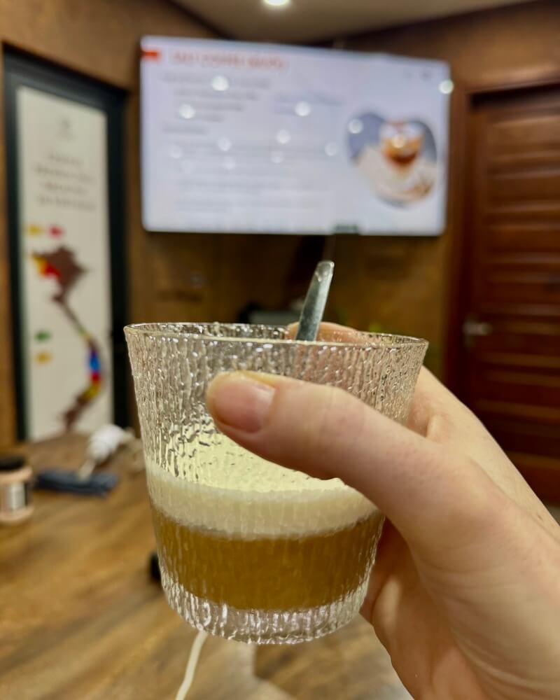 Allison Green's hand holding a cup of salt coffee with a layer of salty whipped cream atop condensed milk and dark coffee