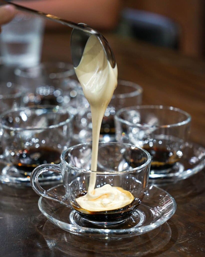 The cream of egg coffee being poured on top of the dark filtered robusta coffee at the bottom of a cup