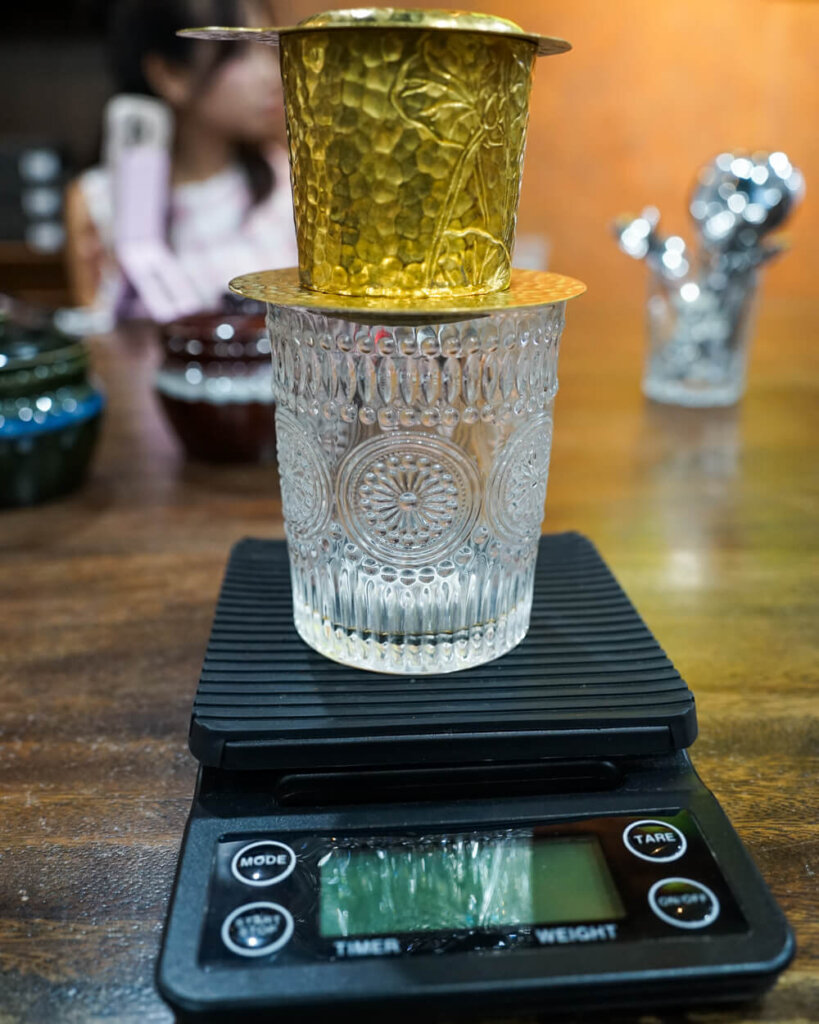 A phin (Vietnamese coffee dripper) on a scale that is used to make accurate timings and pours