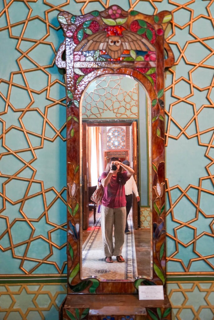 A mirror in the main summer palace room with gold and teal detail and Allison shown in the reflection
