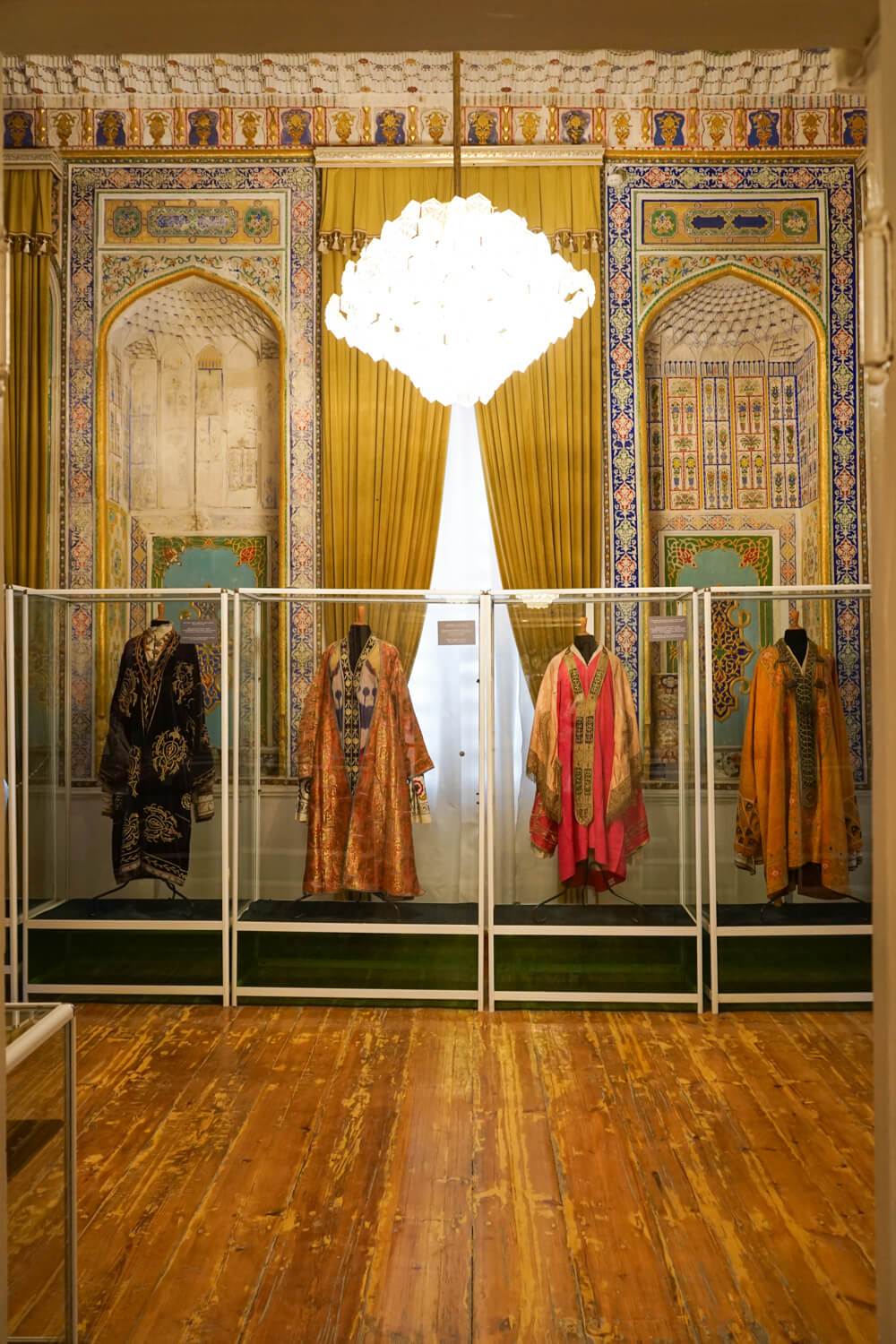 Interior of the national costume museum, with muquarna design, chandelier, and four national costumes displayed in glass boxes