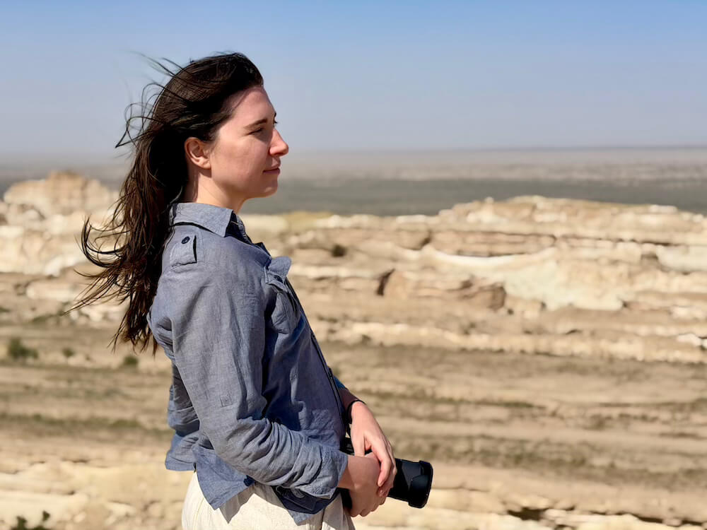 Allison wearing a denim-looking shirt and looking onto a desert landscape with her camera