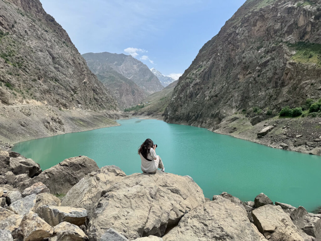Allison sitting and taking a photograph of the beautiful sights around her at the fourth lake, belly button lake, in Tajikistan