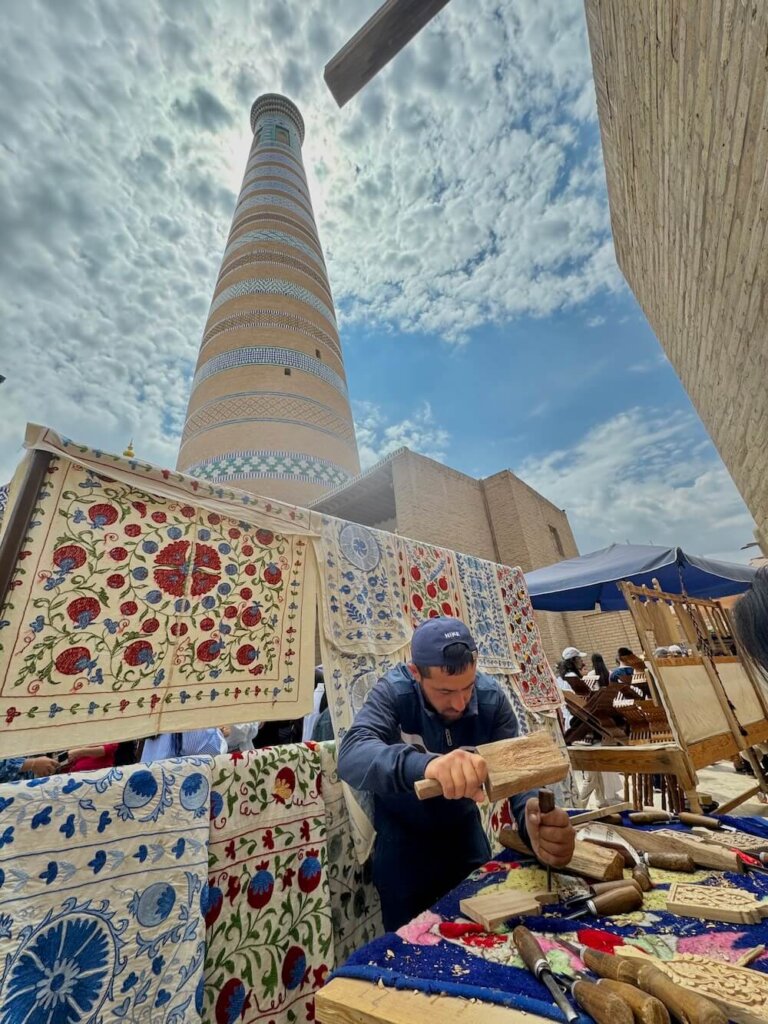 Minaret behind our woodworking master, suzani wall, and our guide helping us make our wood crafts